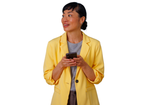 Asian businesswoman in a yellow blazer holding a phone, texting, and looking away with an engaging smile on a transparent background - Powered by Adobe