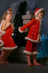 Brother and sister in red elf costumes celebrating Christmas with a large collection of presents near a cozy decorated tree.