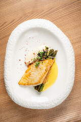 A beautifully plated dish features grilled fish alongside asparagus and a rich sauce