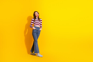 Casual chic young woman model posing in striped top and jeans against a bright yellow background