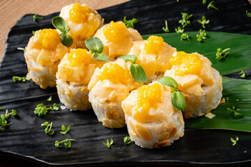 Delicate sushi rolls adorned with mango sauce and fresh herbs sit beautifully on a black platter