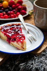 A slice of plum cake sits on a white plate beside a warm cup of tea, surrounded by autumn fruits