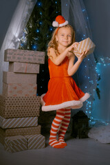 Holiday celebration with a girl in a red Santa outfit holding a Christmas gift surrounded by sparkling decorations.