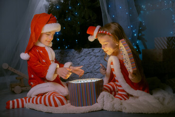 Boy and girl dressed as Santa revealing a bright glowing box, capturing the spirit of Christmas and New Year.