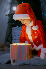 Festive moment of a boy in Santa costume unveiling a glowing gift box under the Christmas tree on a holiday evening.