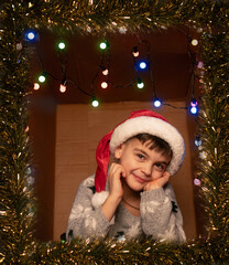 Cheerful child sitting in a decorated box with Christmas lights and tinsel, posing playfully for New Year