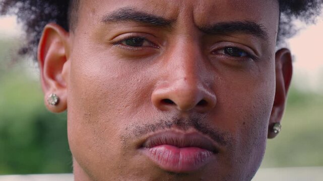 Close up of African American man with curly hair and earrings looking seriously ahead with focused intense expression and furrowed brows outdoors in natural daylight