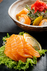 A beautiful display of salmon sashimi alongside a bowl of sushi rolls and pickled ginger