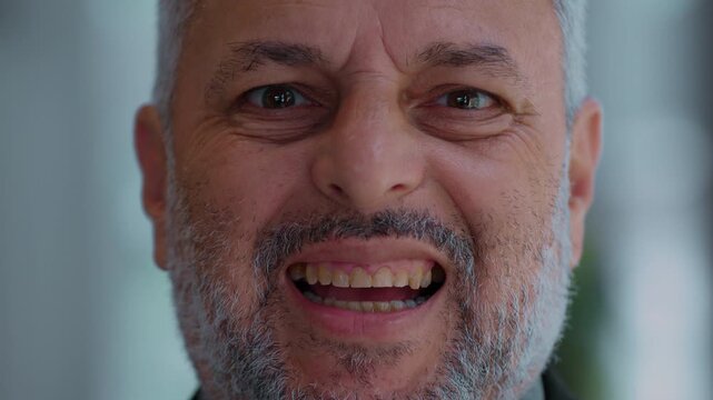 Close up portrait of weary middle aged man with gray beard forcing uneasy smile, showing discomfort and emotional strain beneath surface while trying to appear cheerful