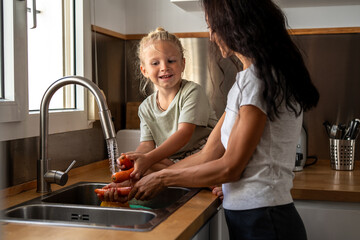 Mother and young boy washing fresh carrots and vegetables under running tap water together in the...