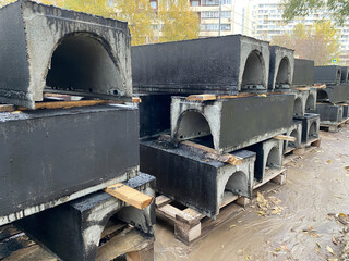 Concrete blocks on wooden pallets awaiting installation. Precast concrete utility trench. Urban road surface repairs, including utility line replacement. Concrete cable channel with waterproofing.