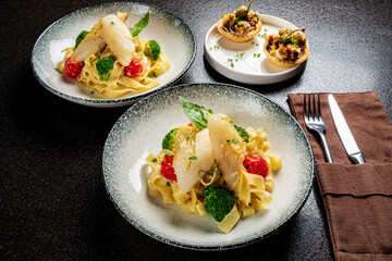 Two bowls of fettuccine with vibrant broccoli and tomatoes served alongside tasty appetizers