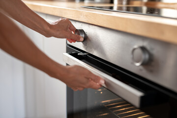Person adjusting temperature knob and opening modern stainless steel oven in kitchen