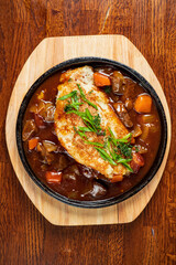 Delicious fish rests on a hearty mix of vegetables and sauce, served hot on a wooden platter