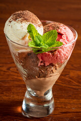 A tasty dessert of chocolate, strawberry, and vanilla ice cream in a glass bowl with mint