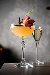 A vibrant cocktail with a floral garnish sits prominently on a bar table, inviting enjoyment