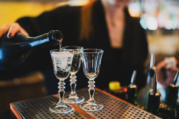 Bartender pouring clear alcohol into elegant shot glasses on a metal bar surface. Close-up shot, vibrant bar atmosphere, preparing drinks, nightlife, service