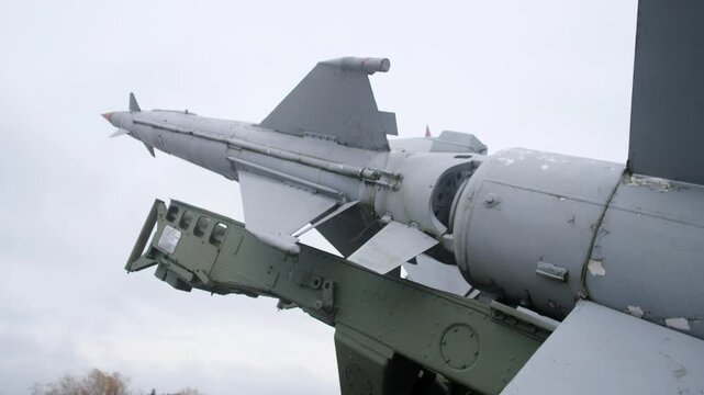 surface missile mounted on angled launcher with visible fins and aft section, grey paint and hardware under cloudy sky; close framing highlights guidance fins, mount assembly and riveted