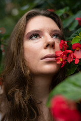 Portrait of a young female musician with long hair near bright red flowers in outdoor setting