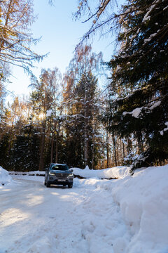 Issyk-Kul, Kyrgyzstan - December 13, 2024: A gray MG RX8 SUV drives on an icy, snow-covered road flanked by tall coniferous and deciduous trees on a bright winter day