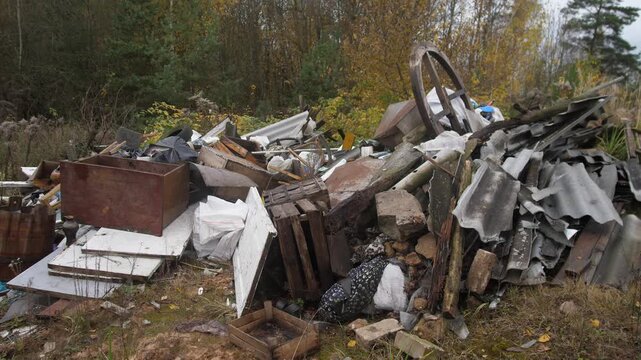 rural illegal dump site with piles of mixed construction debris, wheel and corrugated roofing; contractor surveying scene while municipal inspector documents environmental blight