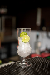 A hurricane glass filled with ice and lemon slices placed on a black bar mat on a bar counter, creating a refreshing mixology setup ideal for cocktail preparation and bar ambience scenes.