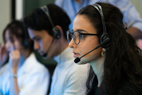 Customer support team in a modern call center receiving guidance from a supervisor. Diverse employees working with headsets and computers, representing teamwork, communication, and  technology.