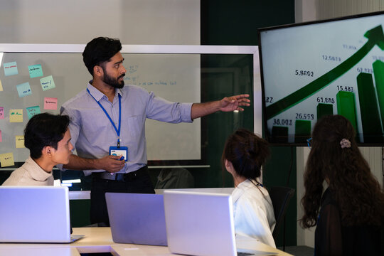 Business team analyzing data on laptops with growth chart in background. Diverse professionals collaborating in office, discussing financial performance, strategy, and success analytics in  workplace.