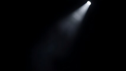 A dramatic stage spotlight cutting through a smoky atmosphere in deep darkness.