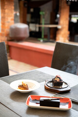 A shot of tiramisu, dark chocolate brownie, and sizzling brownie placed together on a table, served in white plates with a softly blurred restaurant ambiance in the background 