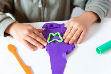 Child pressing green mold into purple clay on white table. Concept of creativity, imagination and fine motor skill development through playful learning.