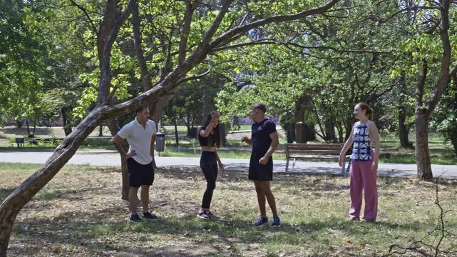 Young adults enjoy a bright day at the park, sharing laughs and engaging in playful activities. One challenges himself by attempting to hang from a tree branch, creating a fun, interactive moment.