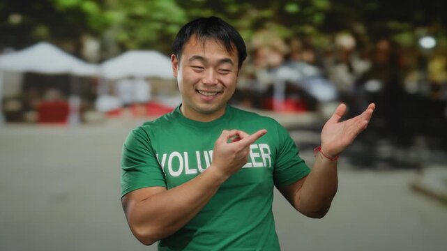 Young man smiling in green volunteer shirt outdoors in urban street setting, showcasing positive charity work.