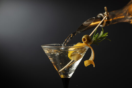 Classic dry martini cocktail with green olives, lemon peel, and rosemary on a black background. - Powered by Adobe