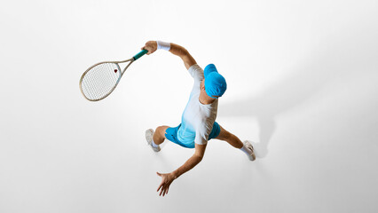 Tennis player in bright blue uniform preparing serve captured from above on white studio floor....