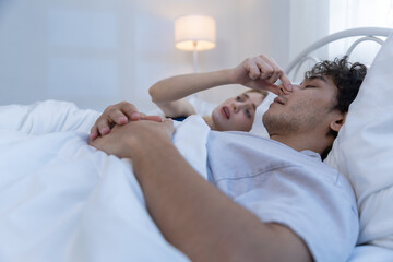 Couple lying in bed, man is picking his nose, and woman next to him looks annoyed. She seems so unpleasant with situation right now