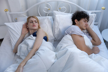 Young couple in bed, faces express frustration and distance. atmosphere in bedroom feels tense and uncomfortable
