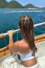 Young woman with braided hair relaxing on a boat, smiling in the warm summer light. Fresh, carefree travel mood on the water with a bright outdoor atmosphere.