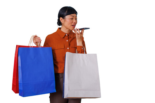 Asian woman shopping using voice assistant on phone while holding colorful shopping bags, transparent background