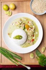 Thai green fish curry served with sticky rice on a wooden board, styled with fresh lemon slices, spring onion and raw rice, creating a vibrant and flavorful Asian food presentation 