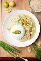 Thai green fish curry served with sticky rice on a wooden board, styled with fresh lemon slices, spring onion and raw rice, creating a vibrant and flavorful Asian food presentation 