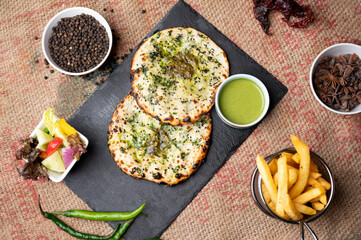 Palak mozzarella kulcha served with mint mayo salad, green chutney and fries, styled with raw garam masala on a rustic sack background for a flavorful Indian street food presentation.