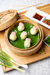 Close-up shot of truffle edamame dim sum placed in a bamboo steamer on a wooden board, beautifully styled with green cut chillies and red chilli sauce, creating a modern Asian gourmet presentation.