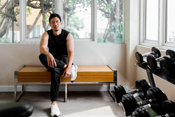 Asian man sitting in gym corner relaxing after workout