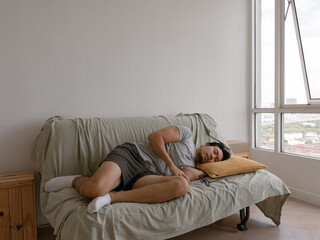 Asian man lying on couch with legs up and face turned sideways in white shirt and clean background