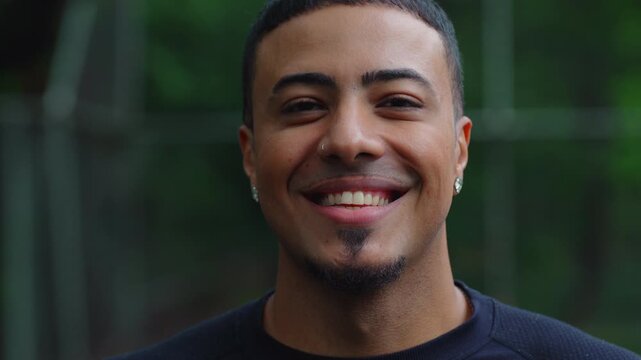 Smiling Latin Hispanic man of African descent with goatee and nose ring standing outdoors, looking directly at camera with joyful friendly expression in natural park environment