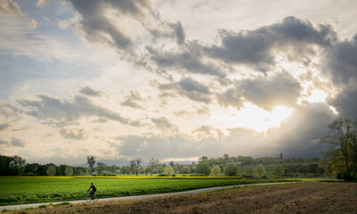Lone rider cycling amid fields with sunbeams through clouds in Switzerland