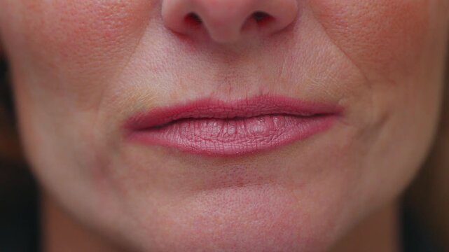 Close-up of woman&rsquo;s lips and lower face with natural lipstick and visible skin texture, expressing quiet composure and maturity