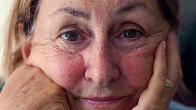 Elderly woman resting her head on hands, looking directly at camera with serene expression, close up of aging face conveying warmth, resilience, and humanity