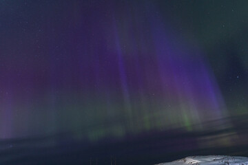 Powerful magenta and violet columns of Aurora Borealis light the starry night sky above a small...